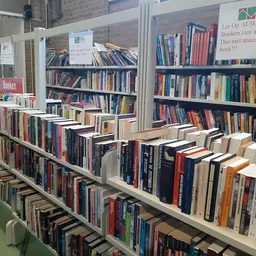 Stellingen vol met tweedehands boeken, gerangschikt op een lange tafel in de winkel