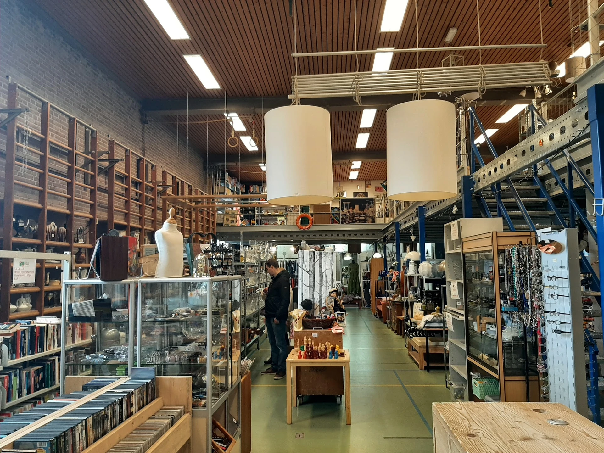 Winkelvloer met stellingen, vitrines en diverse tweedehandsartikelen, grote cilindervormige objecten aan het plafond