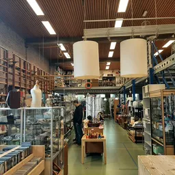 Winkelvloer met stellingen, vitrines en diverse tweedehandsartikelen, grote cilindervormige objecten aan het plafond
