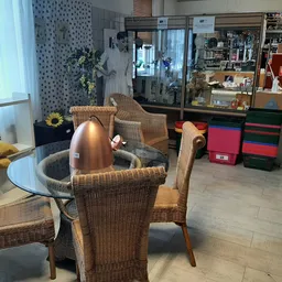 Zithoek met rieten stoelen rond glazen tafel in kringloopwinkel met stellingen op achtergrond