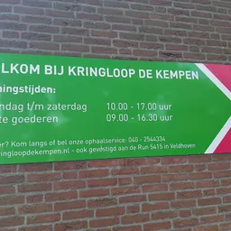 Groen en roze welkomsbord met openingstijden en contactgegevens van kringloopwinkel
