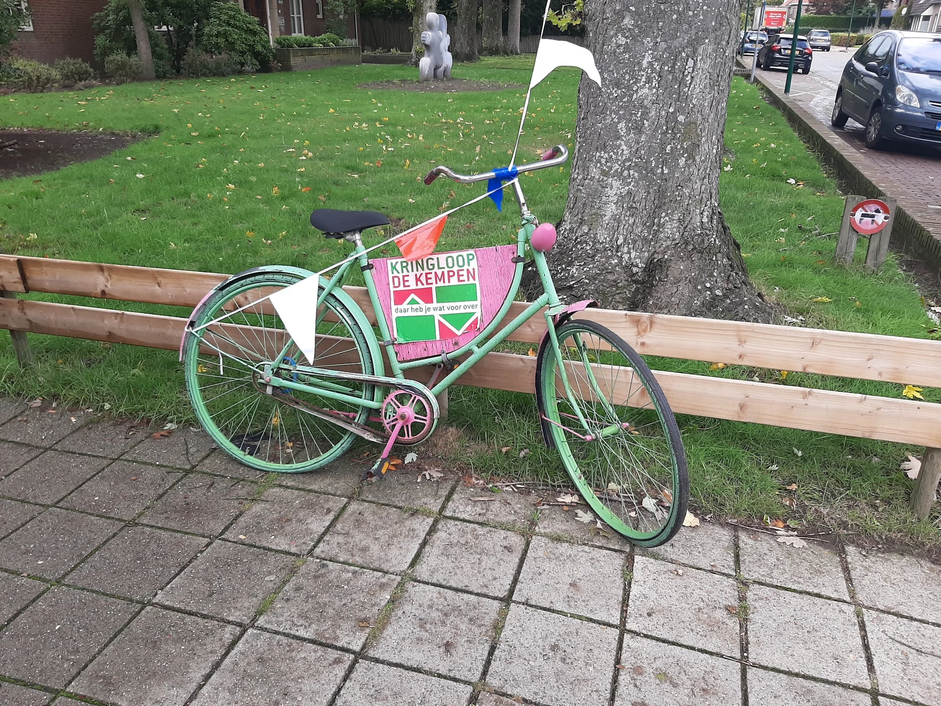 Groen vintage damesfietsen met roze zadel en stuur, tegen houten bankje op patio