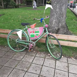 Groen vintage damesfietsen met roze zadel en stuur, tegen houten bankje op patio