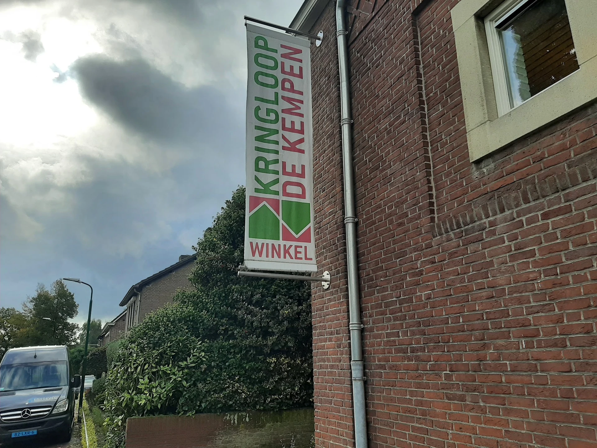 Voorgevel van kringloopwinkel met groen-wit bordje 'Kringloop de Kempen Winkel' tegen bakstenen muur