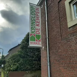 Voorgevel van kringloopwinkel met groen-wit bordje 'Kringloop de Kempen Winkel' tegen bakstenen muur