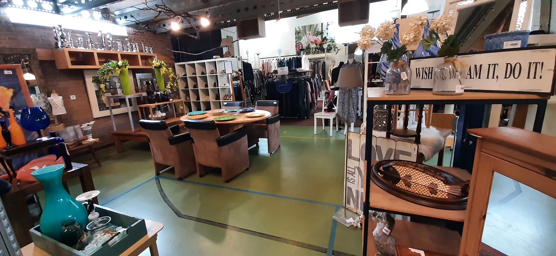 Winkelvloer met bruine stoelen rond tafel, kledingrekken, stellingen en diverse tweedehands artikelen