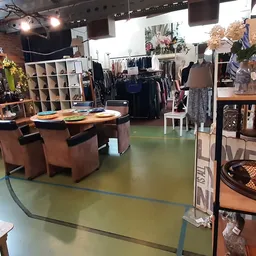 Winkelvloer met bruine stoelen rond tafel, kledingrekken, stellingen en diverse tweedehands artikelen