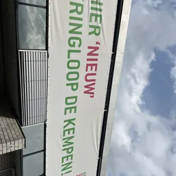 Zijkant van winkelgevel met wit doek waarop groene en rode tekst 'Kringloop De Kemp' zichtbaar