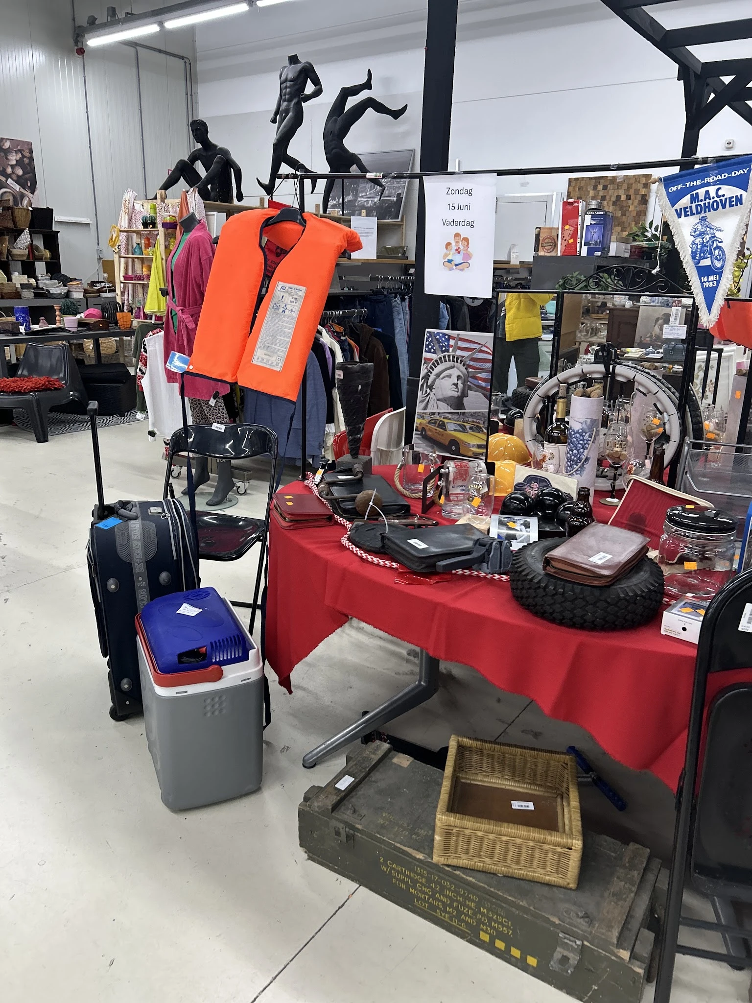Rode toonbanktafel met tweedehands artikelen zoals schoenen, accessoires en huishoudspullen, met kleding en fietsen op de ach