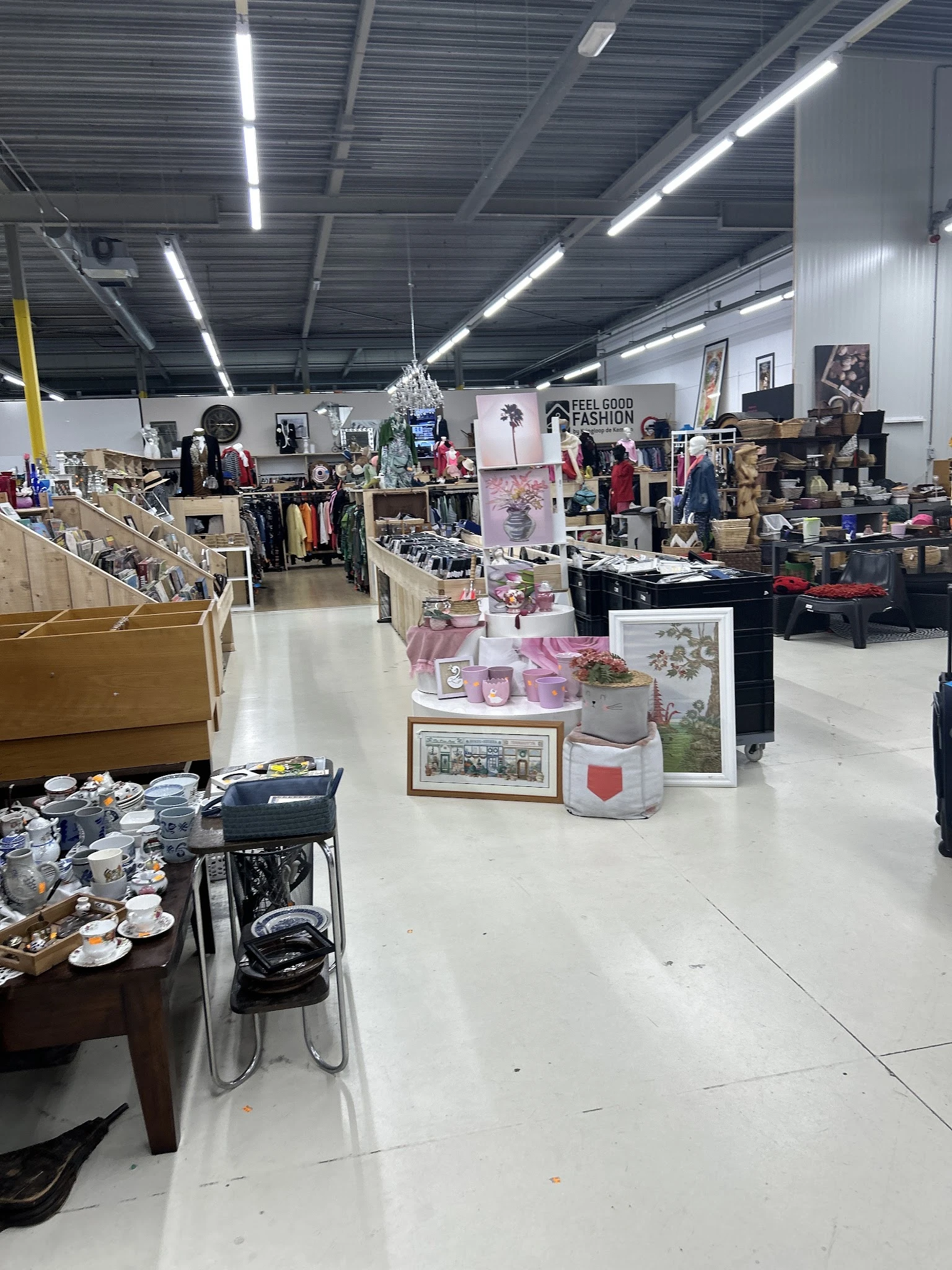 Ruim winkelbinnenruimte van kringloopwinkel met diverse uitgestalde spullen, rekken met kleding, decoratieartikelen en meubil