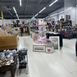 Ruim winkelbinnenruimte van kringloopwinkel met diverse uitgestalde spullen, rekken met kleding, decoratieartikelen en meubil