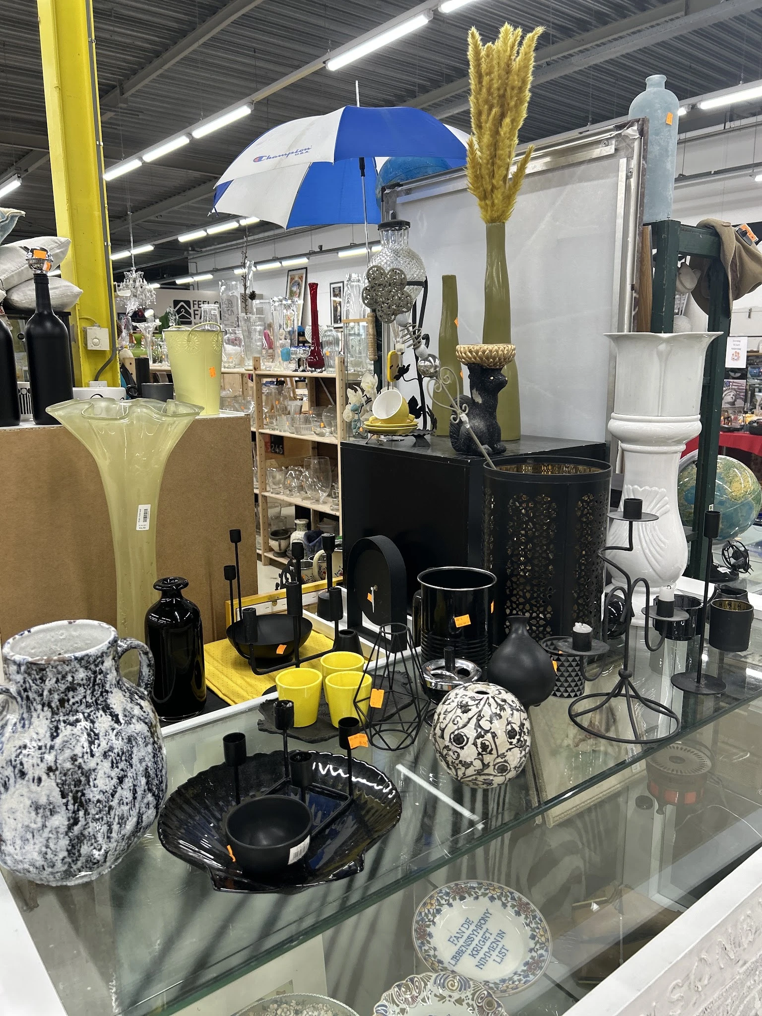 Uitgestalde decoratieve items en huishoudwaar in zwart en geel, waaronder vazen, kaarsen, schalen en kunstobjecten