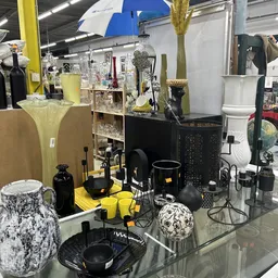 Uitgestalde decoratieve items en huishoudwaar in zwart en geel, waaronder vazen, kaarsen, schalen en kunstobjecten