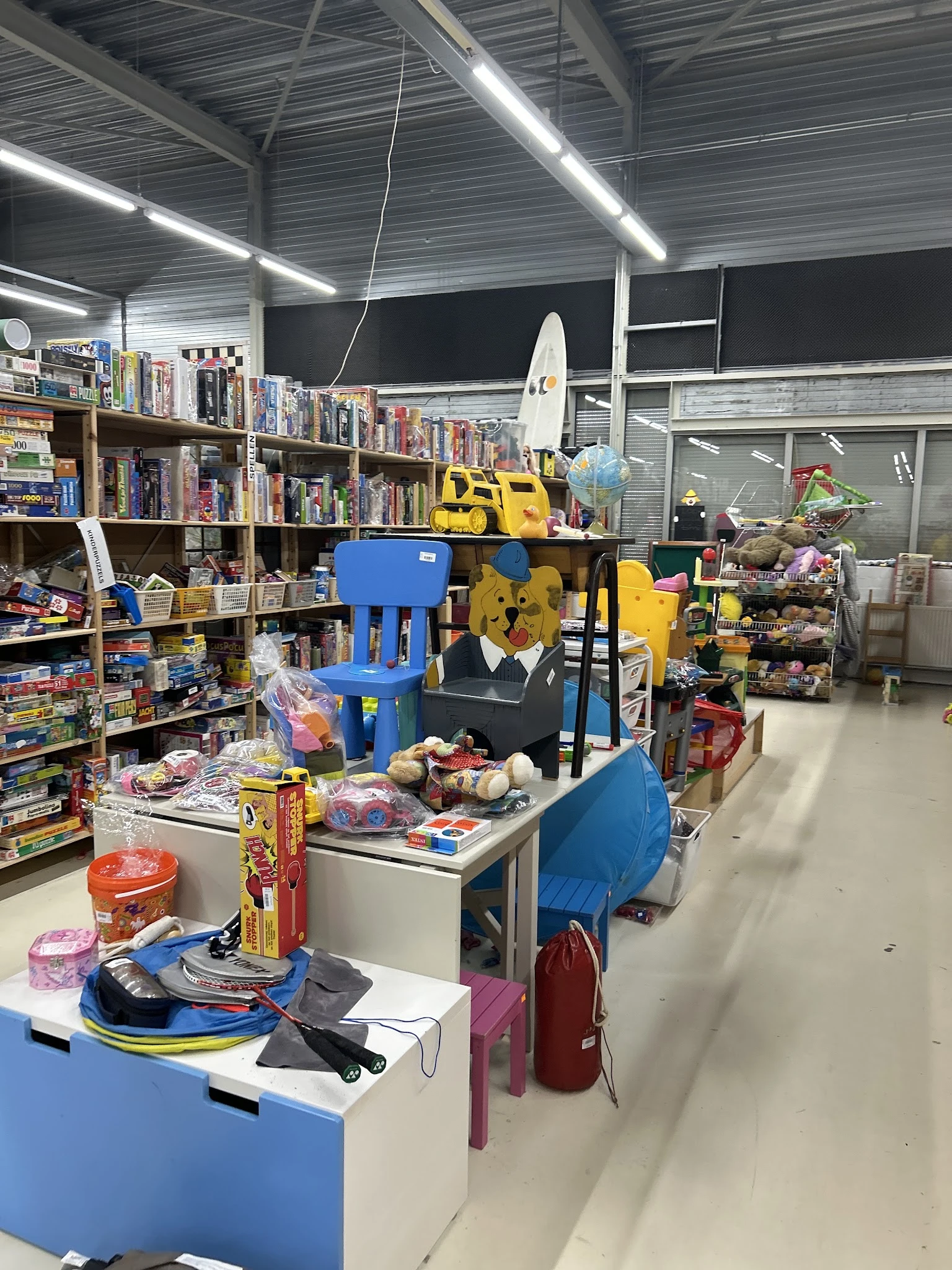 Winkelvloer met speelgoed, gele kindervoertuigen, blauwe stellingen en schappen vol spullen
