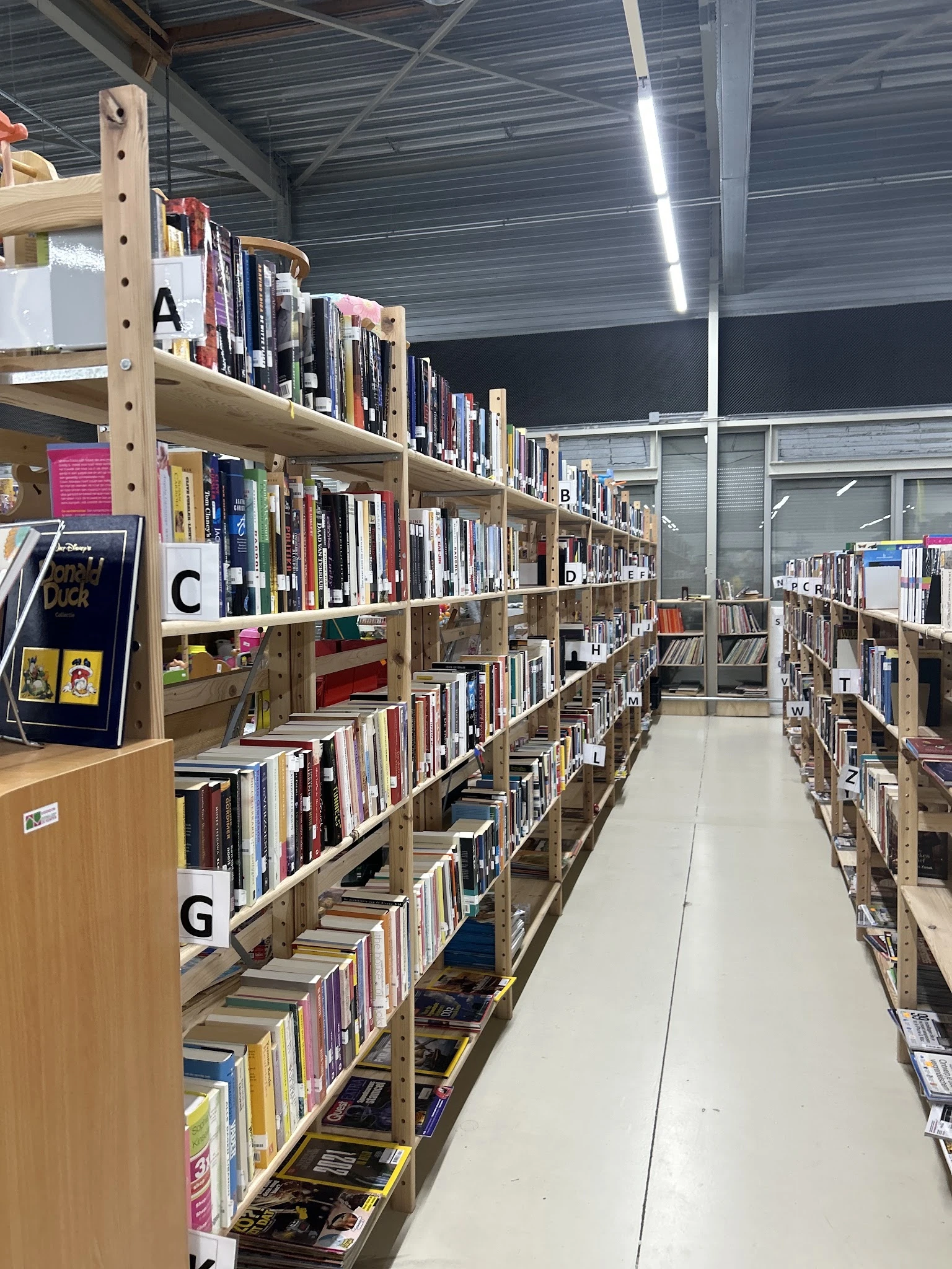 Boekenkasten met boeken gesorteerd op alfabet in een kringloopwinkel, met gangpad in het midden