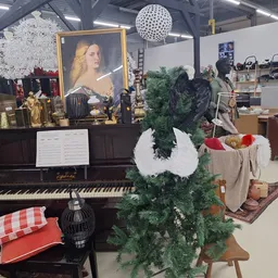 Interieur van kringloopwinkel met een zwarte vleugel, kerststukken, groene slinger en diversen inrichtingsartikelen