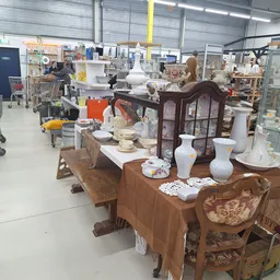 Winkelvloer met houten meubels, serviesgoed en huishoudelijke artikelen uitgestald op tafels en in vitrines