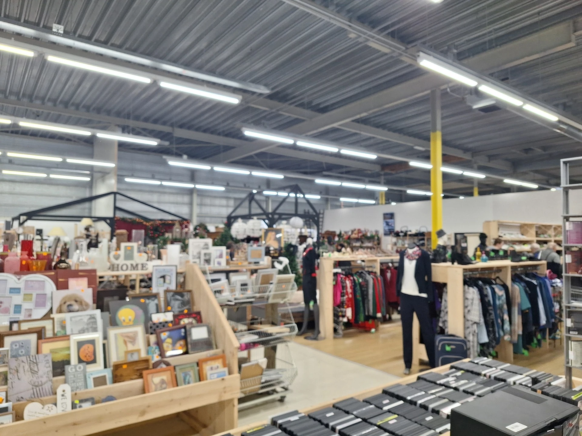 Overzicht van de winkelvloer met diverse afdelingen: kleding aan rekken, huishoudwaar, kunst en kunstnijverheid, in een groot