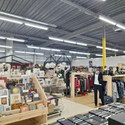 Overzicht van de winkelvloer met diverse afdelingen: kleding aan rekken, huishoudwaar, kunst en kunstnijverheid, in een groot