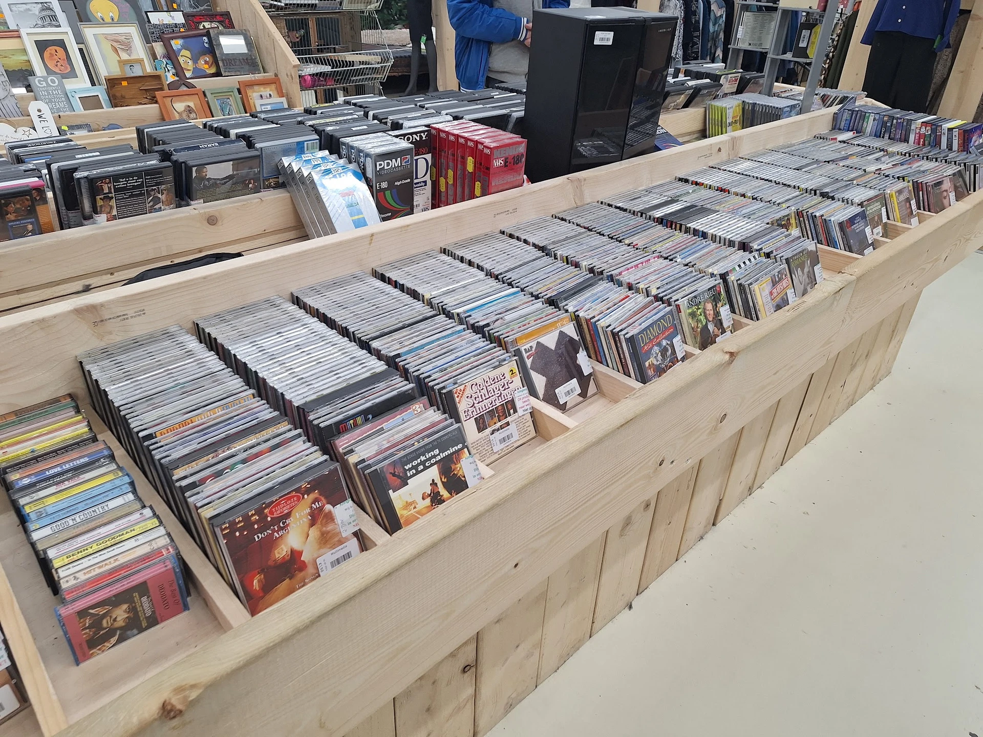 Uitgestalde verzameling cd's en dvd's in dozen en bakken op houten display in kringloopwinkel