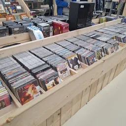 Uitgestalde verzameling cd's en dvd's in dozen en bakken op houten display in kringloopwinkel