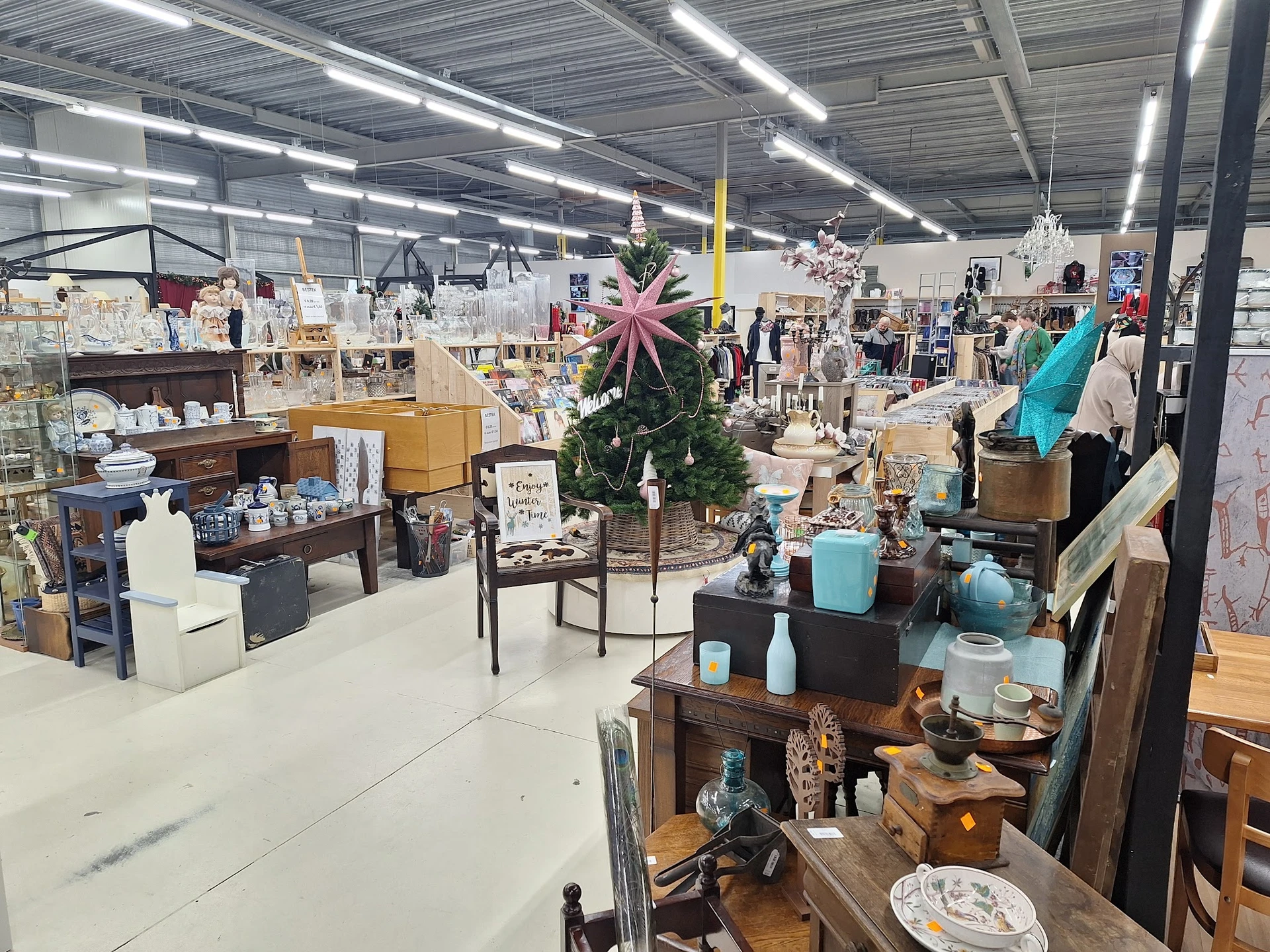 Overzicht van de kringloopwinkel met meubels, decoratie, servies en huishoudelijke artikelen uitgestald op verschillende nive