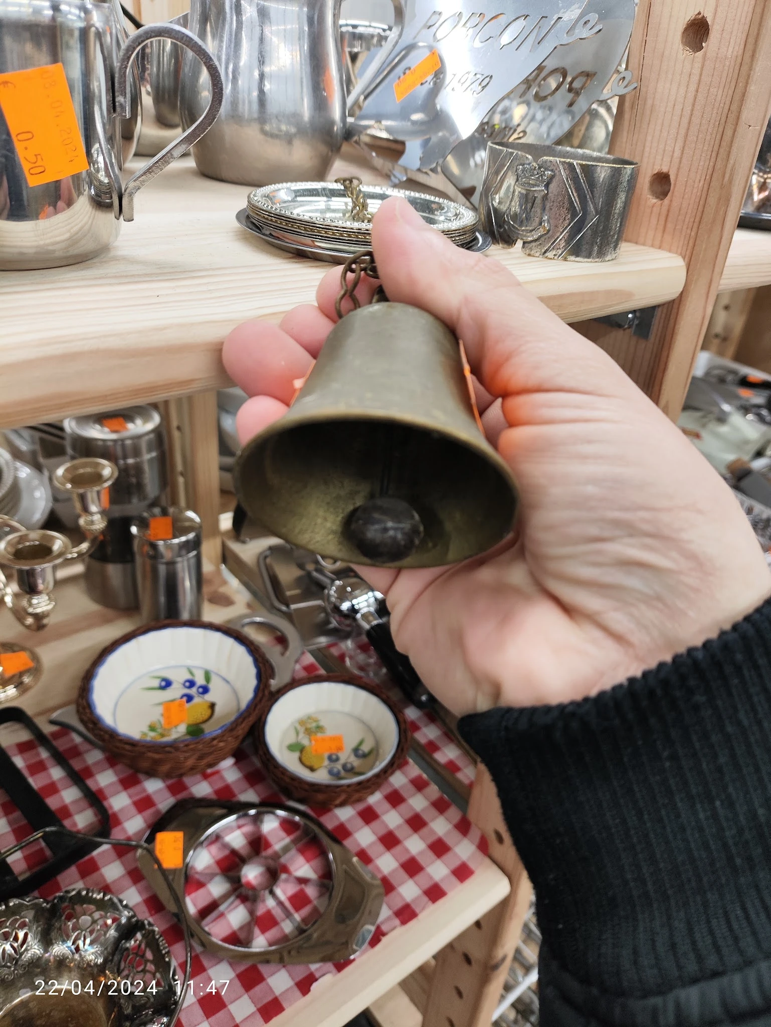 Hand houdt een grijze keramische bel omhoog, met serviesgoed met bloemenpatroon zichtbaar op achtergrond