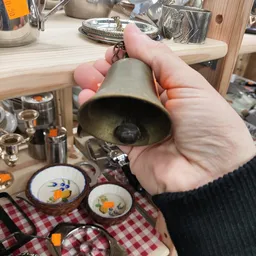 Hand houdt een grijze keramische bel omhoog, met serviesgoed met bloemenpatroon zichtbaar op achtergrond