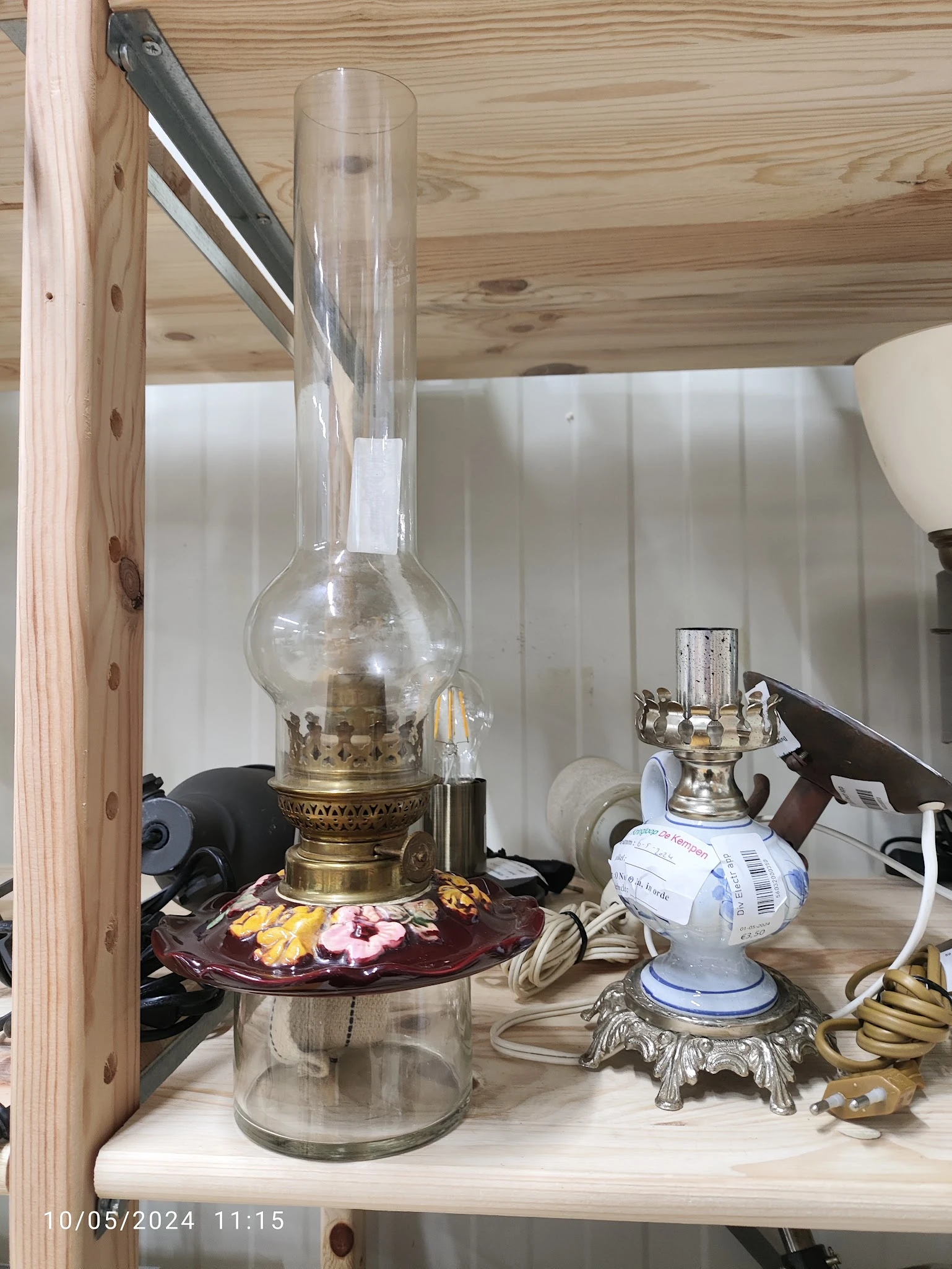 Vintage olielamp met messing fitting en glazen kap op een plank met andere huishoudelijke spullen