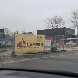 Gele bedrijfsbord van Lamers Aannemingsbedrijf voor een pand met bouwmateriaal op het terrein