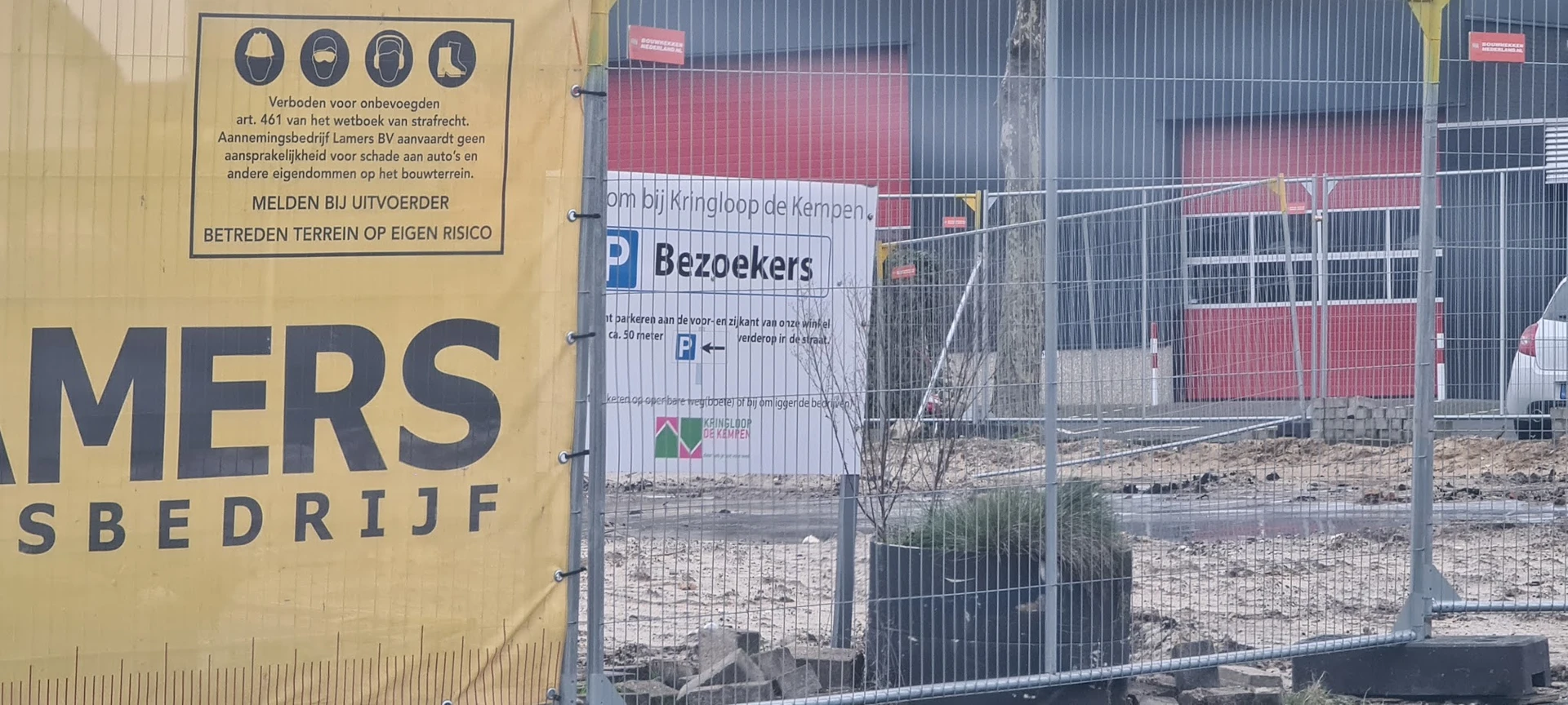 Ingang van kringloopwinkel met parkeerplaatsen-bord, gedeeltelijk verborgen door hekwerk en obstakels
