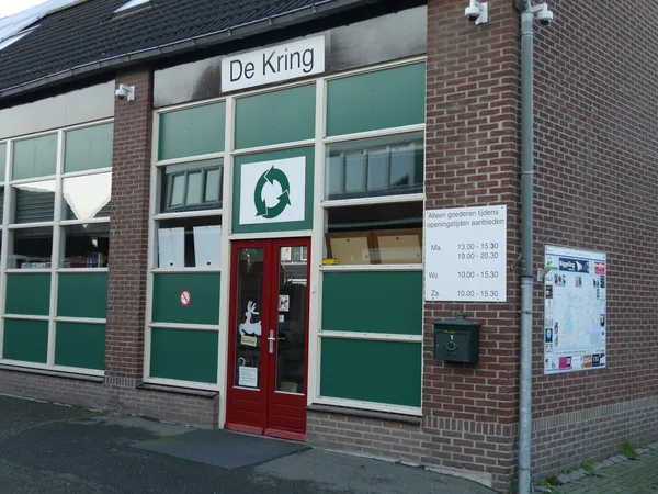 Voorgevel van kringloopwinkel met groene en rode deuren, grote ramen en winkelnaam boven de ingang