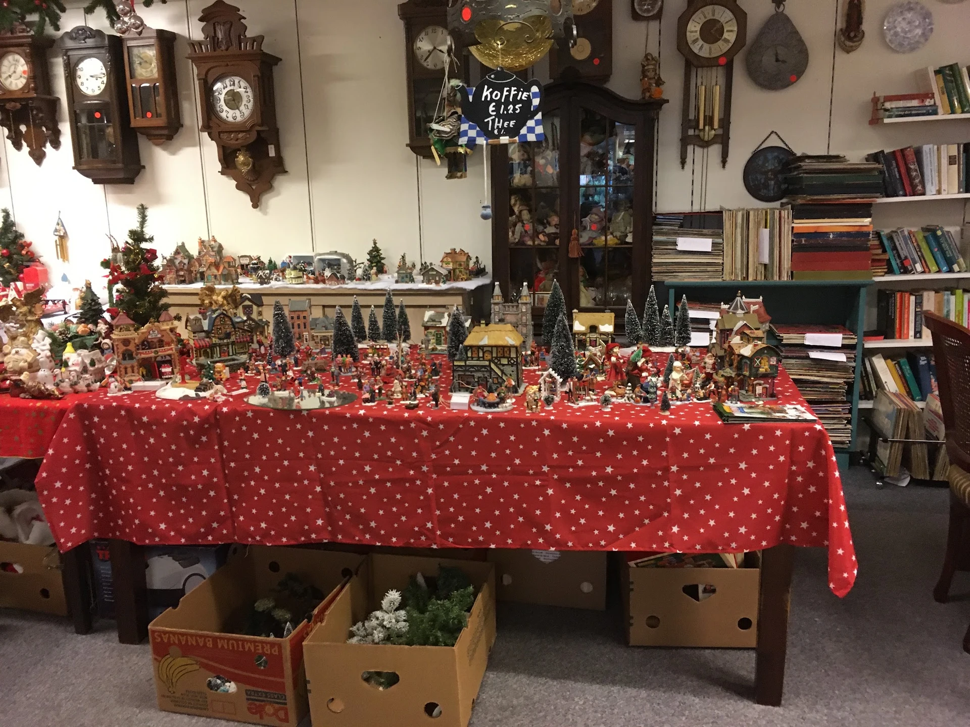 Uitgestalde kerstdecoratie en miniatuurbouwsels op een rode tafel met witte stippen in een kringloopwinkel
