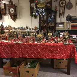 Uitgestalde kerstdecoratie en miniatuurbouwsels op een rode tafel met witte stippen in een kringloopwinkel