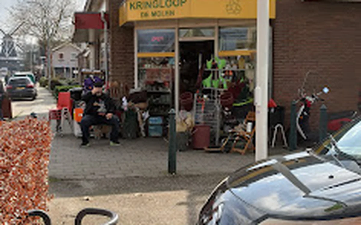 Voorkant van kringloopwinkel De Molen met gele gevel, ingang en uitgestalde spullen op het terras