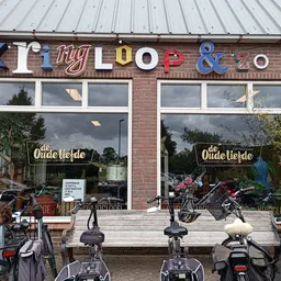 Gevel van kringloopwinkel met gekleurde letters en grote ramen, fietsen geparkeerd ervoor