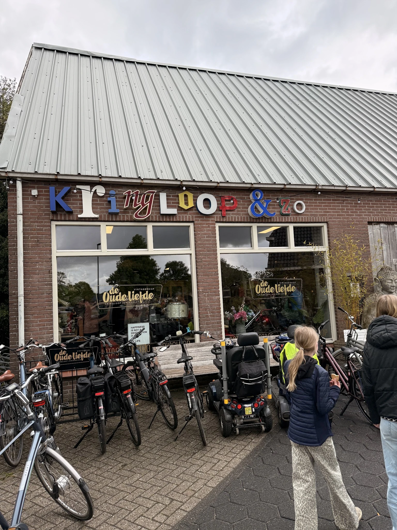 Voorgevel van kringloopwinkel met gekleurde letters, ramen en fietsen geparkeerd ervoor