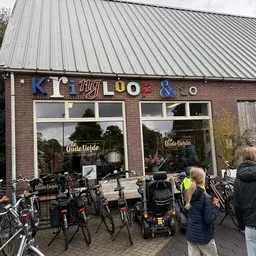 Voorgevel van kringloopwinkel met gekleurde letters, ramen en fietsen geparkeerd ervoor
