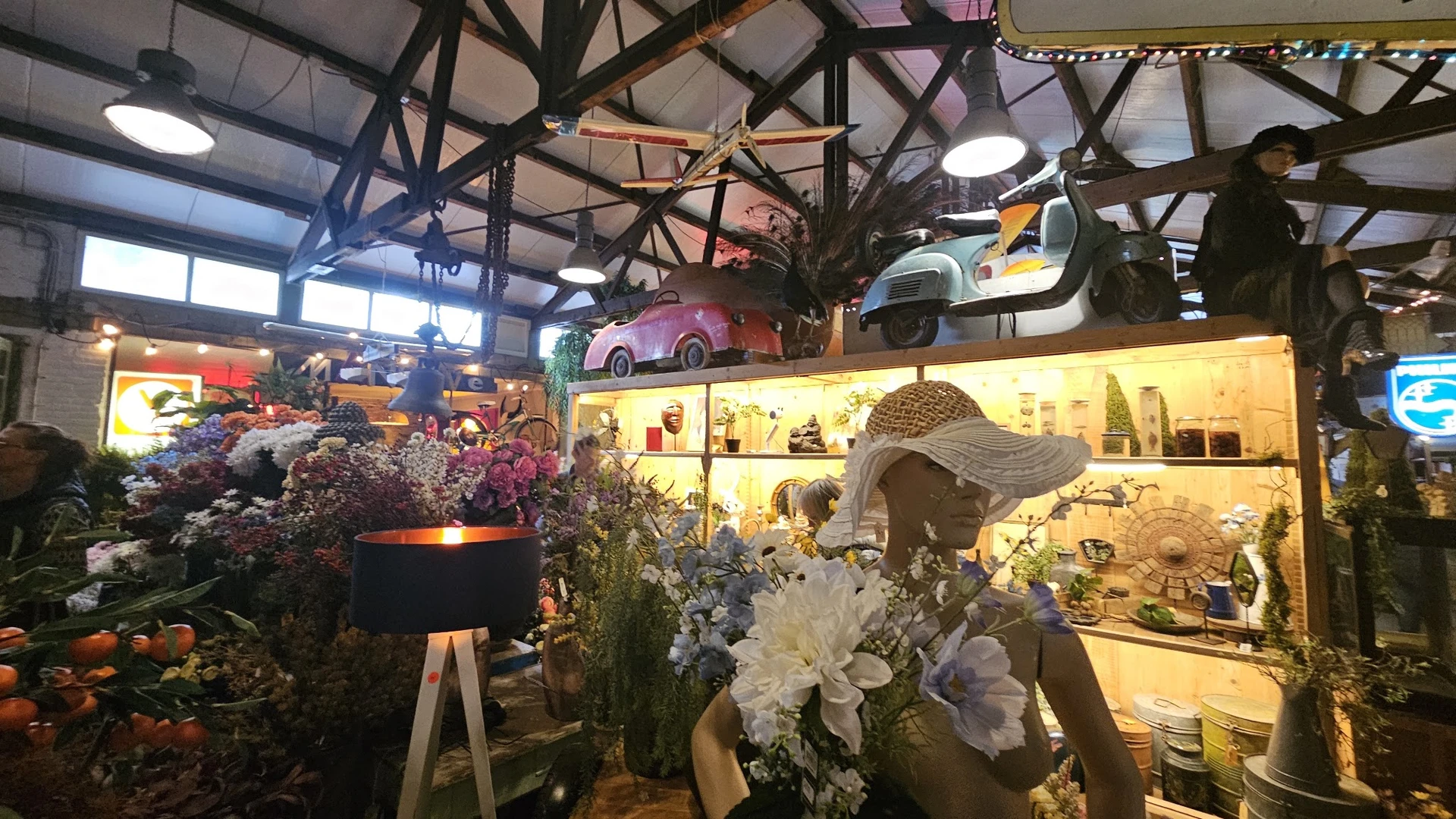 Winkelinterieur met vintage scooters aan het plafond, bloemendecorstukken, verlichte vitrinekast en industrieel dakframe