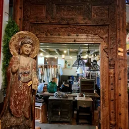 Winkelinterieur met houten deurlijst, boeddhabeeld, hanglampen en rekken met kleding