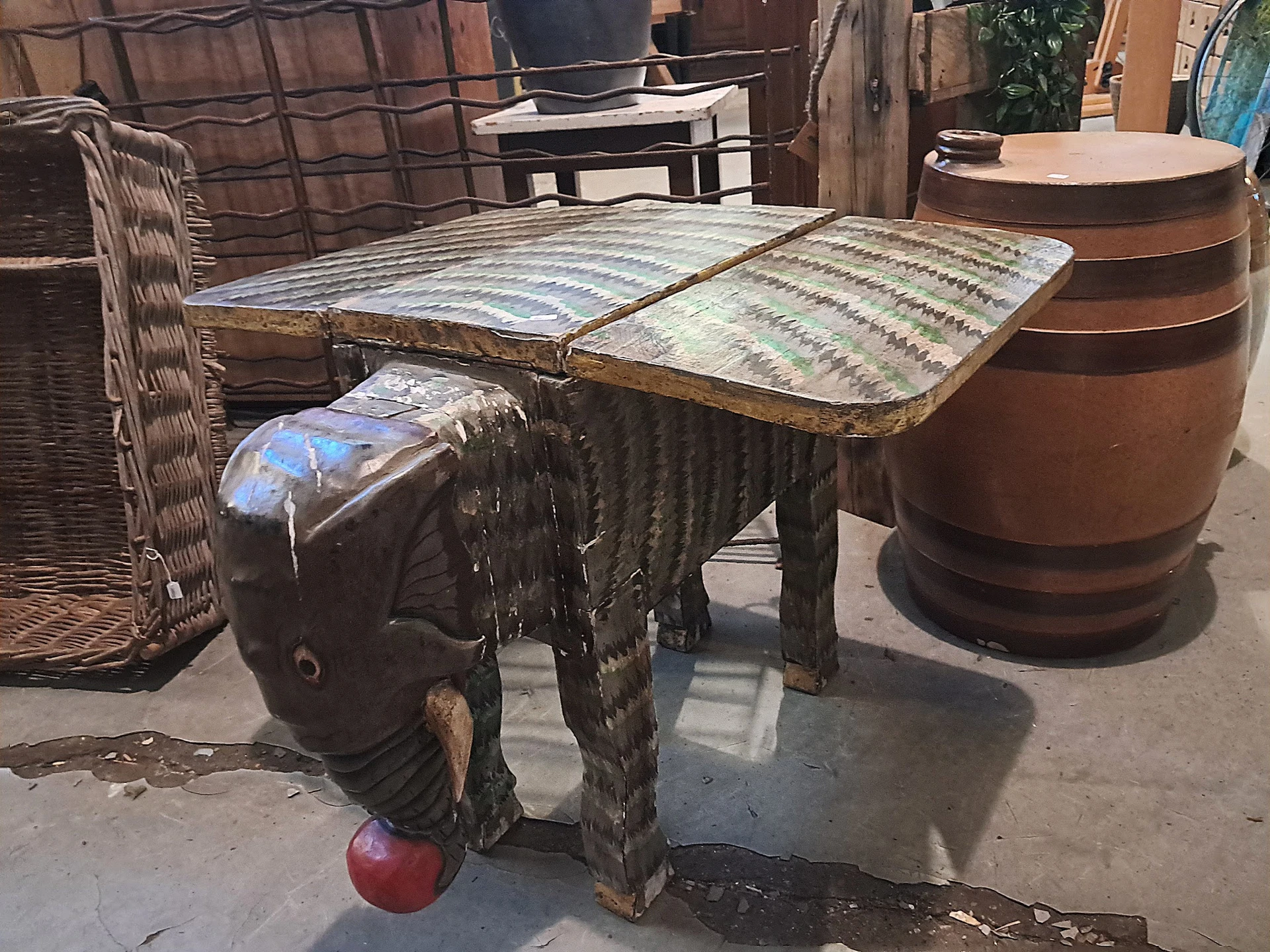 Tweedehands meubels op een terras, onder meer een houten tafel en een bruine ton