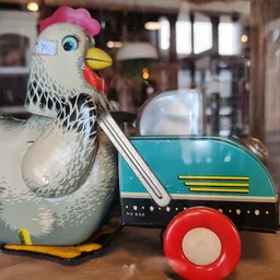 Vintage speelgoed: wit-zwarte kippen-vormige trekauto met roze muts en blauwe aanhanger met rode wielen