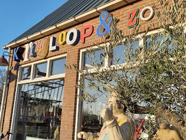 Gevel van kringloopwinkel met rode letters 'KRINGLOOP' en nummer, grote etalageramen met poppen en vintage spullen