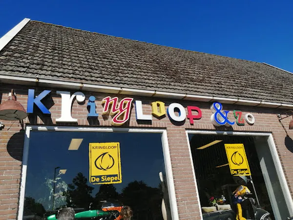 Gevel van kringloopwinkel met gekleurde letters 'King op & co' op rode bakstenen muur, twee etalageramen met spiegeling