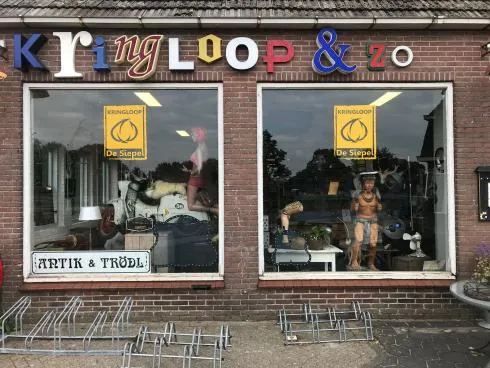 Winkelgevel met bakstenen voorgevel, twee grote etalagevensters met vintage en tweedehands spullen, en gekleurde letters van 
