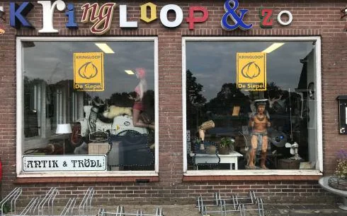Winkelgevel met bakstenen voorgevel, twee grote etalagevensters met vintage en tweedehands spullen, en gekleurde letters van 