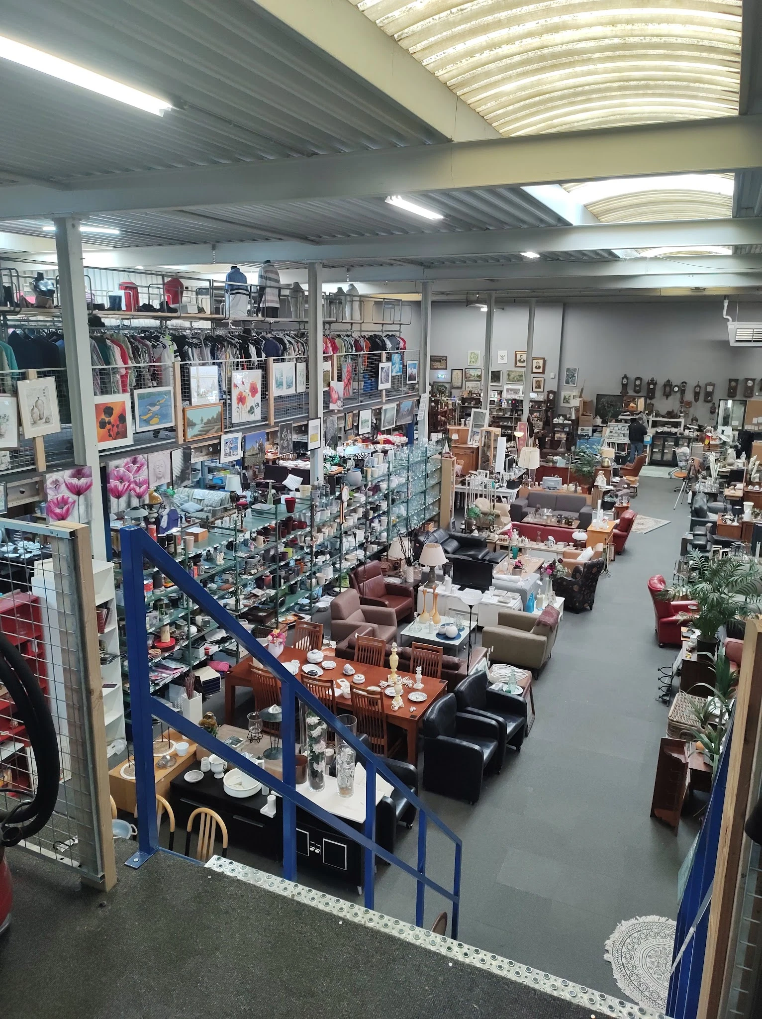 Overzicht van de winkelvloer met meubels, rekken met kleding, kunstwerk aan de muren en diverse spullen uitgestald