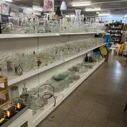 Uitgestalde glazen vazen, kannen en decoratieve items op witte stellingen in de kringloopwinkel