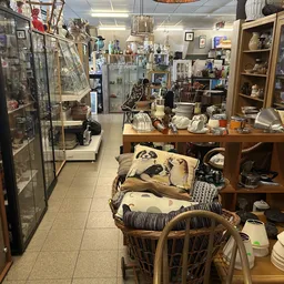 Winkelvloer met houten tafels, stoelen, serviesgoed en huishoudartikelen in stellingen langs de wanden