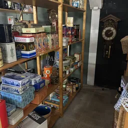 Houten stellingen vol met diverse tweedehands spullen: servies, decoratieve dozen, boeken, een klok en andere verzamelaars it